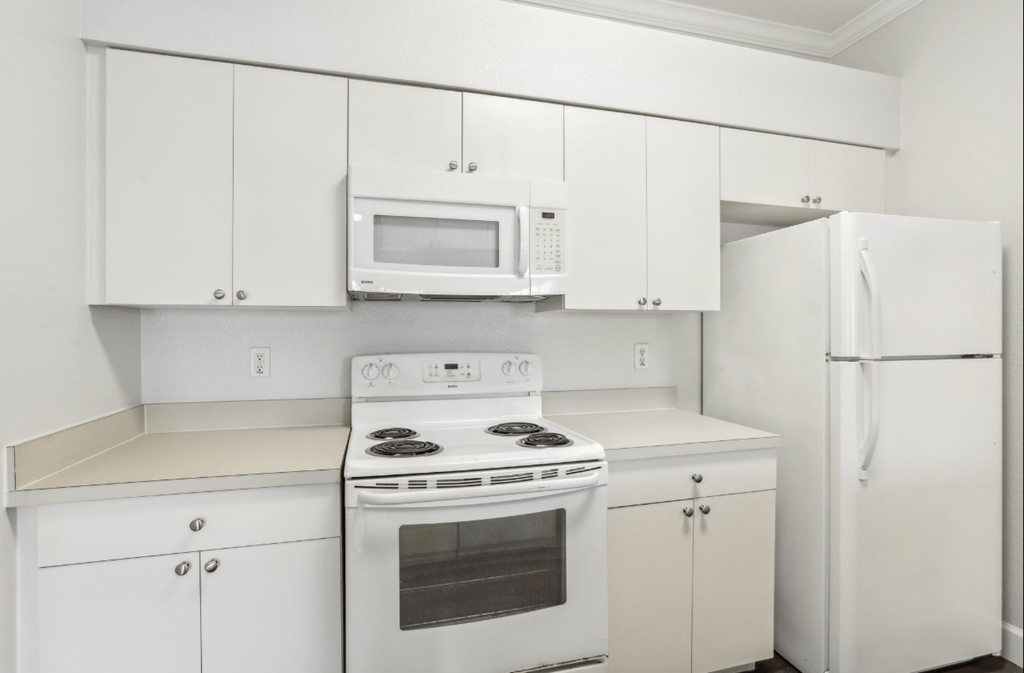 A white kitchen with a stove, microwave, and refrigerator.